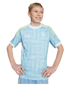 Smiling boy standing with hands on hips, wearing a light blue Juventus football jersey with yellow stripes on the shoulders.