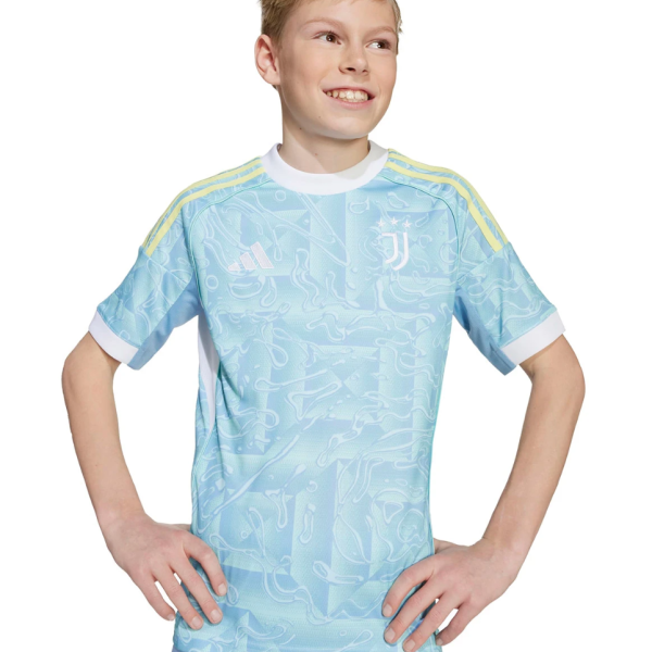 Smiling boy standing with hands on hips, wearing a light blue Juventus football jersey with yellow stripes on the shoulders.