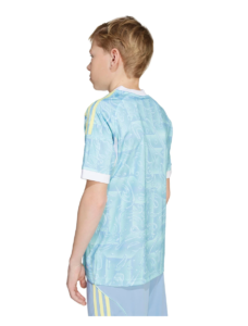 Back view of a young boy wearing a pale blue sports jersey with white cuffs and subtle abstract patterns; yellow shoulder stripes.