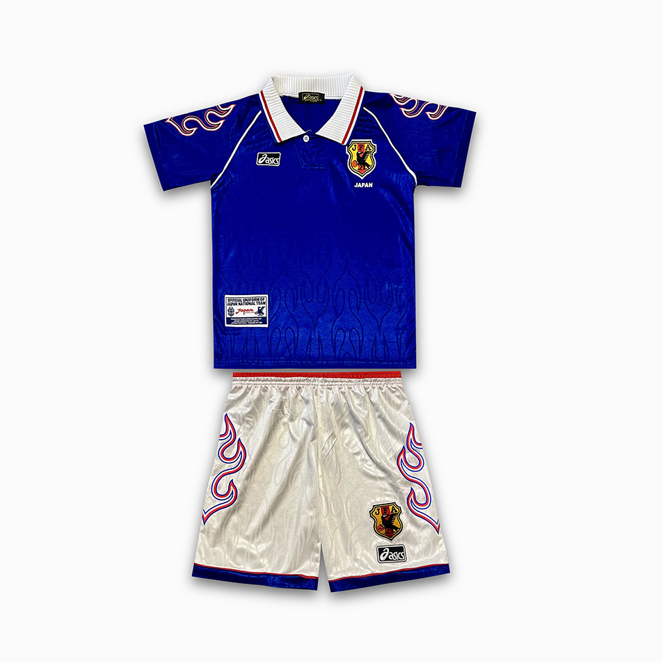 Screenshot_2025-07-08_173950 Blue soccer jersey with Japanese crest and white collar paired with white shorts featuring red-blue flame motifs and team badges, laid flat as a set for kids.