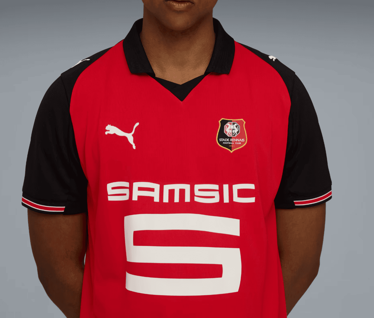 Portrait of a person wearing a red and black Rennes football club jersey with the Puma logo and SAMSIC sponsor text visible on the chest.