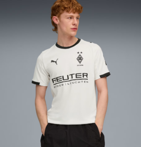 Young man wearing a white Borussia Dortmund football jersey with black trim and sponsor logo, standing with hands in pockets.
