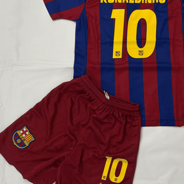 Barcelona soccer jersey with Ronaldinho 10 in yellow on a blue-and-maroon striped shirt, laid over maroon shorts with the club crest and a yellow 10.