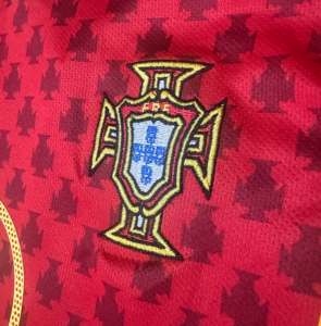 Close-up of a red football jersey featuring the embroidered Portugal Football Federation crest in gold and blue.
