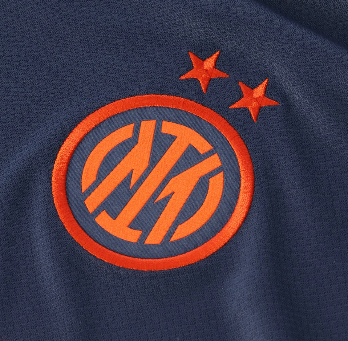 Screenshot_2025-10-12_200444 | UAE SPORT STORE Close-up of navy fabric with an orange circular embroidered team logo and two stars above it.