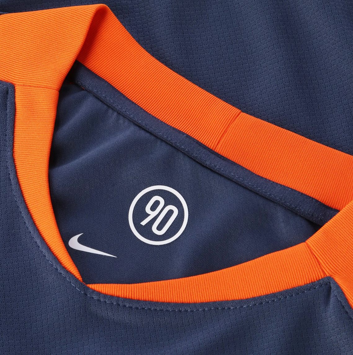 Screenshot_2025-10-12_200503 | UAE SPORT STORE Close-up of navy sports jersey collar in orange with a white Nike swoosh and a circular '90' emblem.