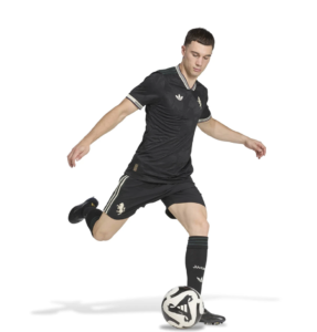 Soccer player in black kit kicking a ball on white background, mid-action pose