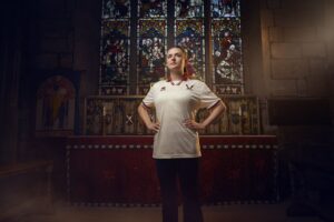 Woman in a white polo stands with hands on hips in a church, in front of an ornate altar and stained-glass window in the background.