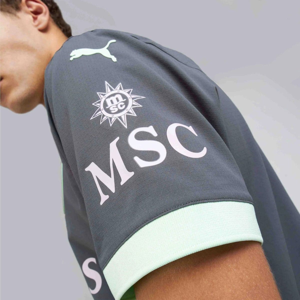Gray athletic sleeve with a white Puma logo and an MSC sun emblem, mint-green cuff visible on the edge.