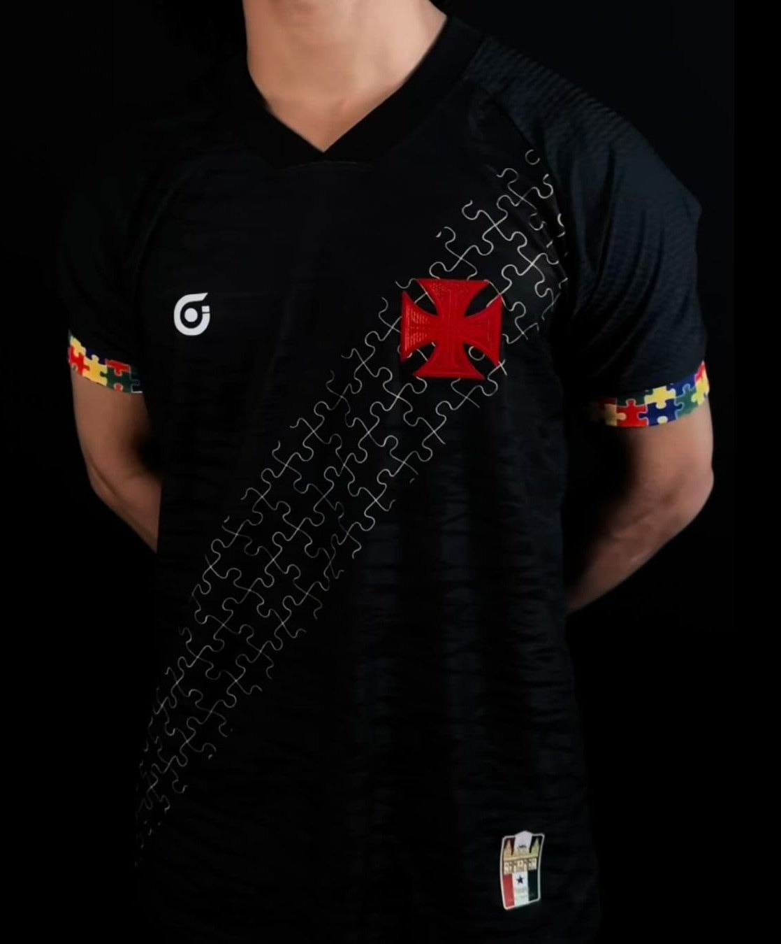 T1CRUioz5T09g9q | UAE SPORT STORE Person wearing a black sports jersey with a red cross badge on the left chest and a diagonal puzzle-piece stripe across the torso.