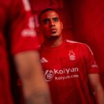 Close-up of a man in a red football jersey looking upward, with a Forest crest on the chest and a red background.