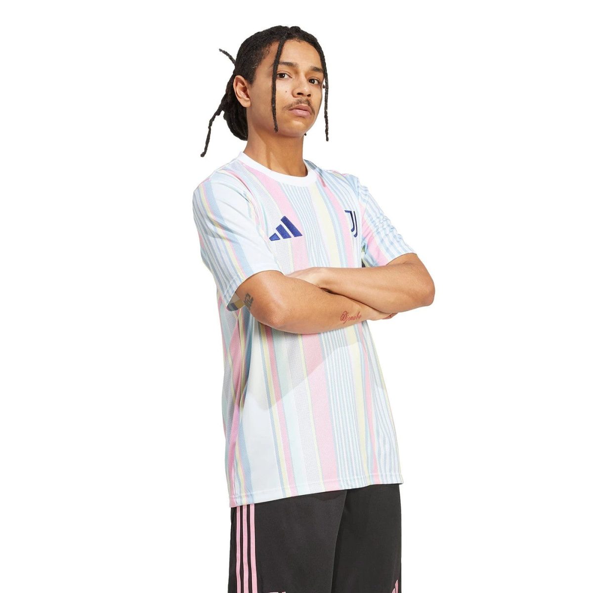 Man with braided hair wearing a pastel striped Juventus Adidas soccer jersey, arms crossed.