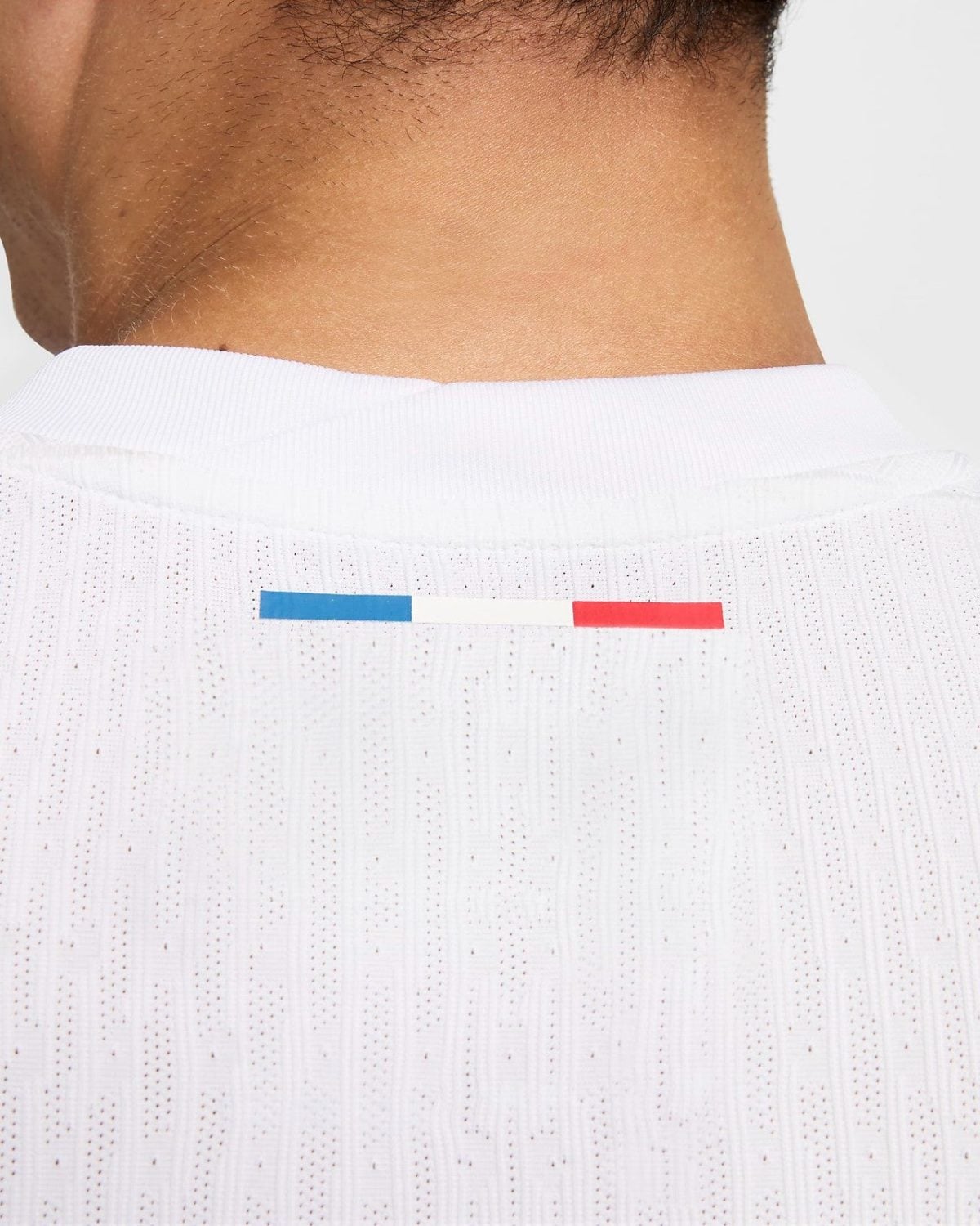 Back of a white sports jersey with a small blue‑white‑red stripe at the neckline, viewed from behind.