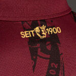 Close-up of maroon fabric with a gold 'SEIT 1900' logo and a stylized bull head graphic.