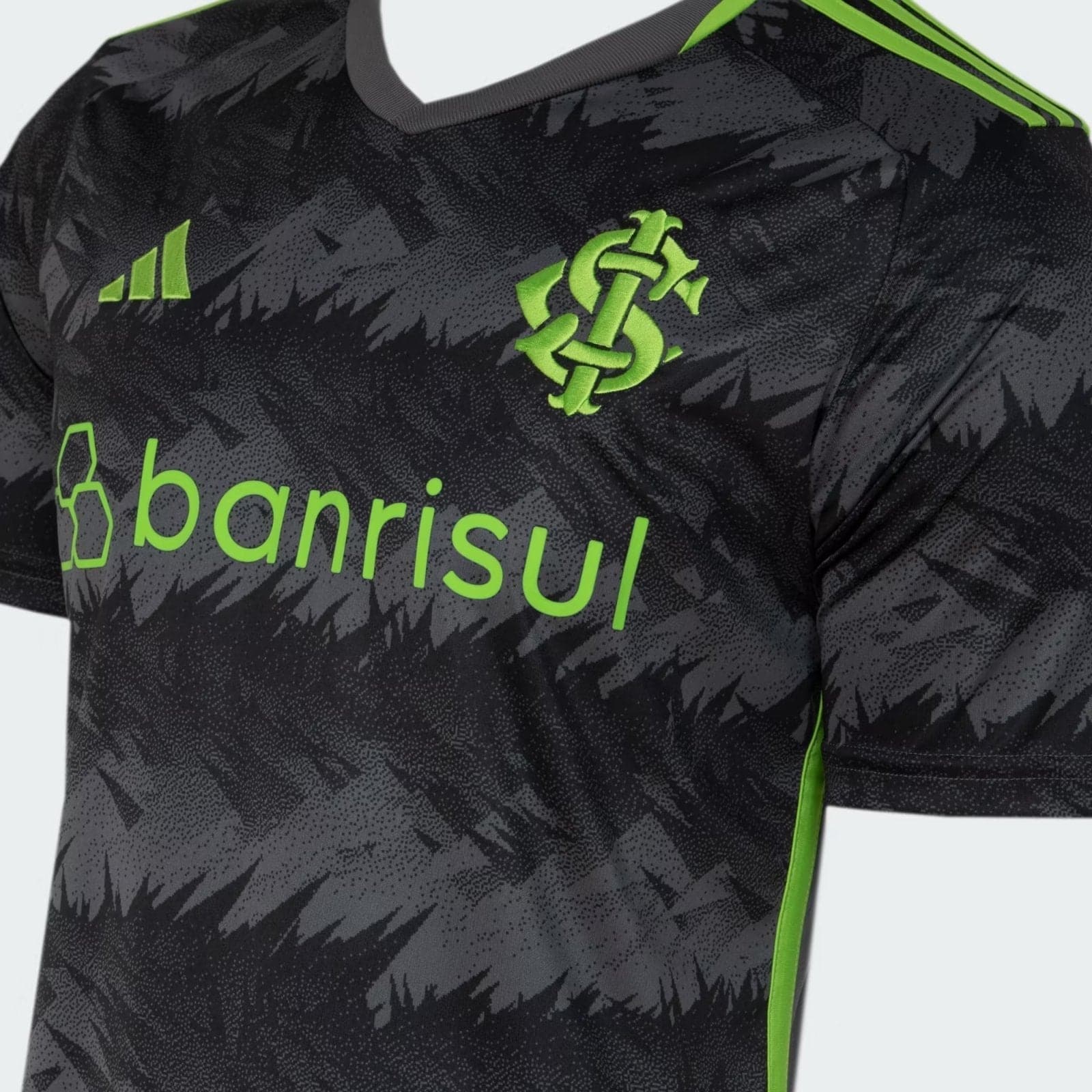 TPYvHyyENZud8cH_74b9bfdd-3faa-4b33-8878-d5b00b754d6d | UAE SPORT STORE Close-up of a dark patterned sports jersey with neon green accents, sponsor text 'banrisul' across the chest and a bright green knot crest on the chest leftside.