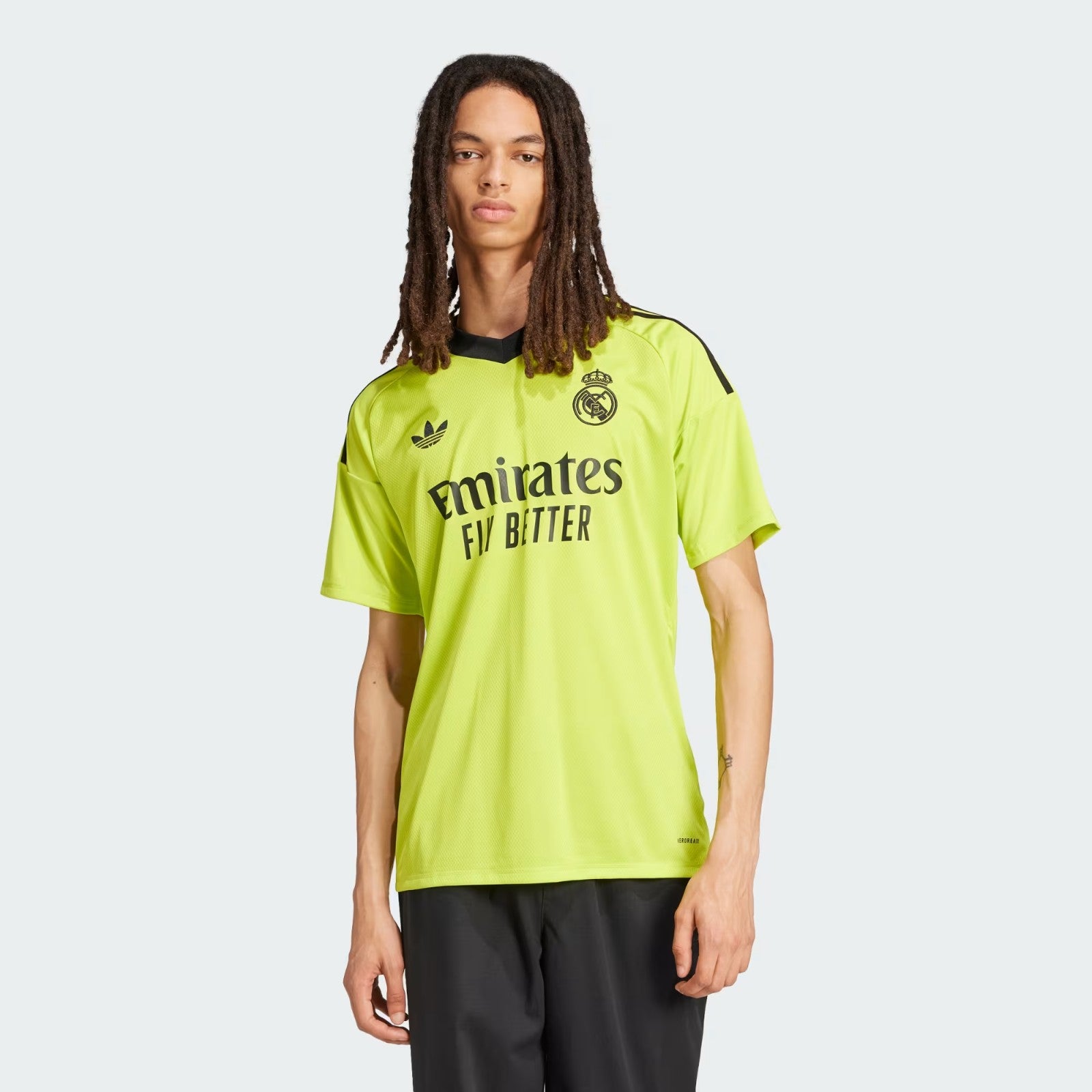 TPruZXCoqhhayEM | UAE SPORT STORE Young man in a neon yellow Real Madrid soccer jersey with crest and 'Emirates Fly Better' sponsor, standing against a pale background.