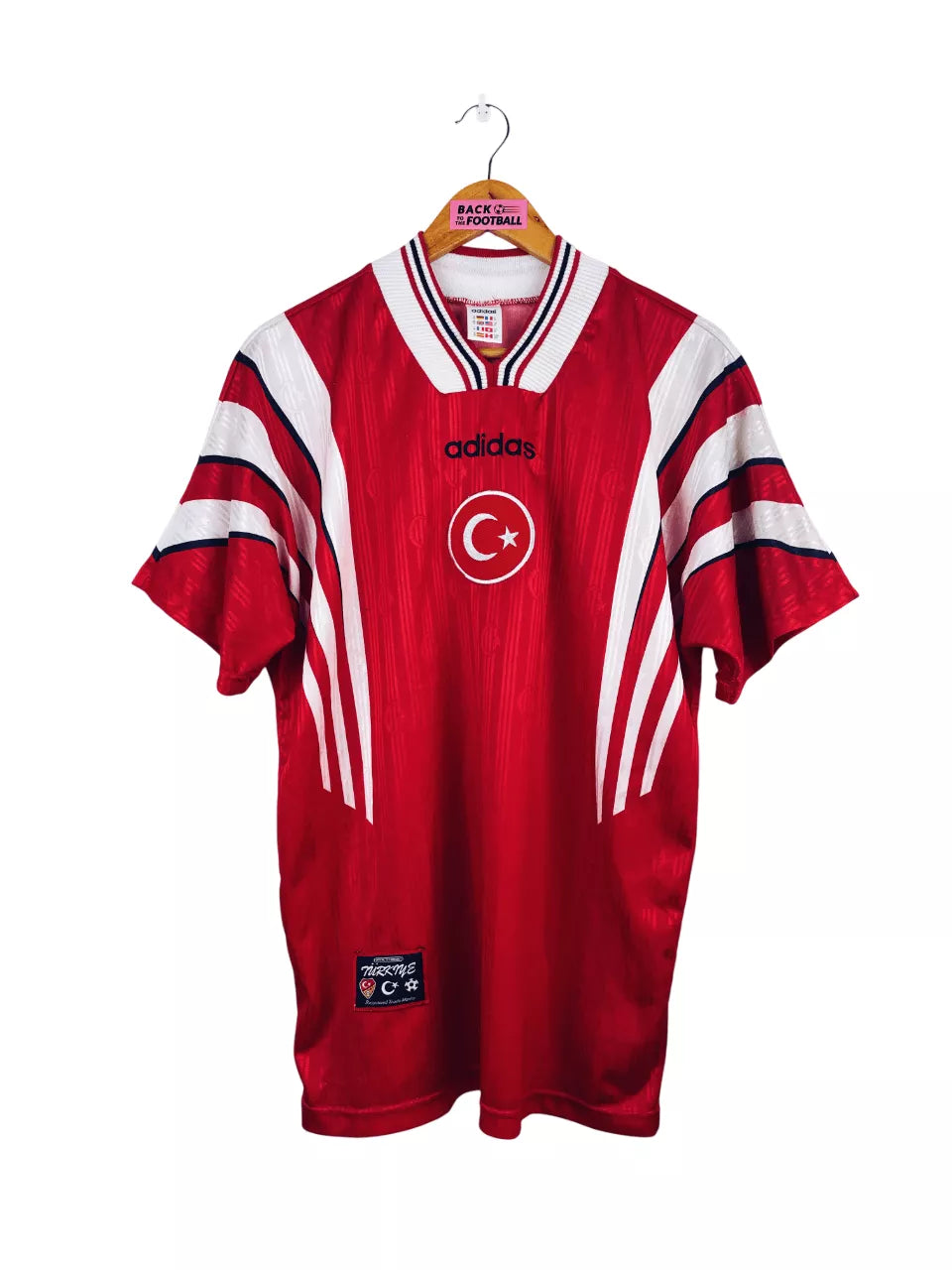 TURQ02_1 | UAE SPORT STORE Red Adidas football jersey hanging on a wooden hanger, featuring a white crescent and star emblem and bold white stripes on the sleeves with Turkish branding.