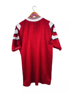 TURQ02_2 | UAE SPORT STORE Back view of a red football jersey hanging on a wooden hanger, with white and navy striped sleeves visible.