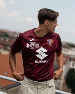 Young man in a maroon Torino FC jersey stands on a rooftop with hands on hips, looking to the right.