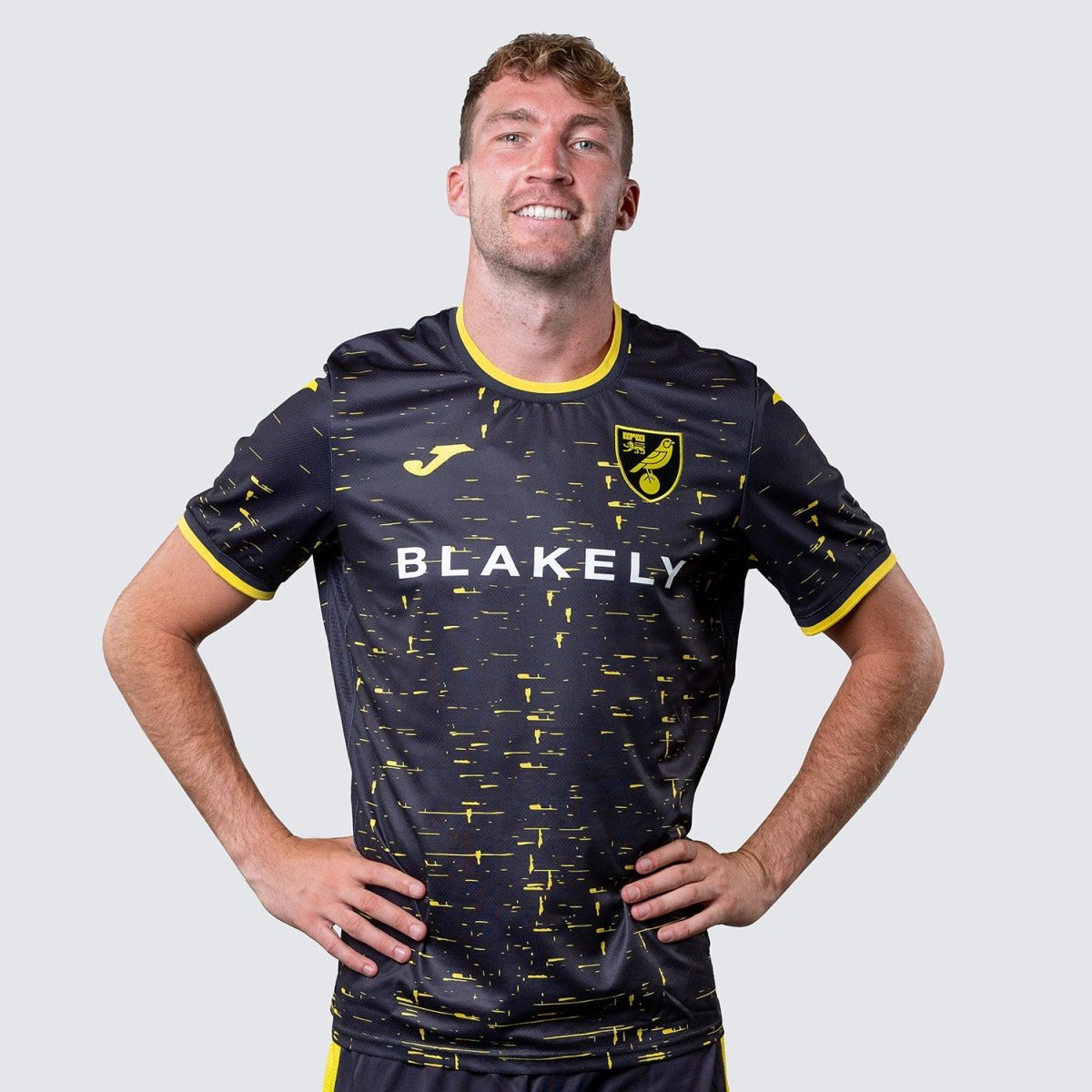 Male soccer player in navy jersey with yellow trim and speckled pattern; 'BLAKELY' sponsor text and team crest.