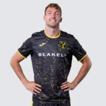 Male soccer player in navy jersey with yellow trim and speckled pattern; 'BLAKELY' sponsor text and team crest.