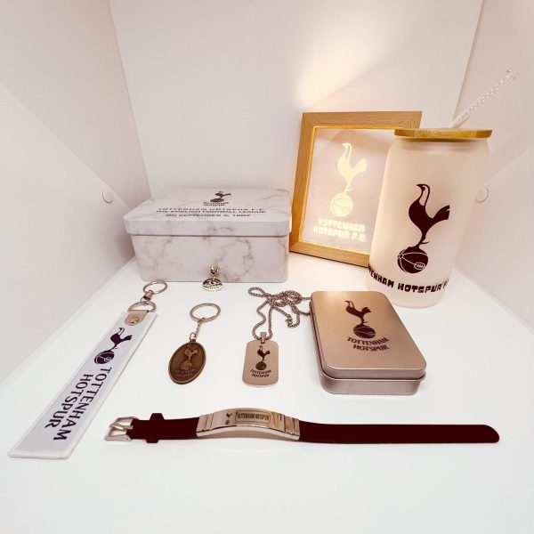 Collection of Tottenham Hotspur merchandise on a white shelf, including keychains, a metal tin, a tumbler, and a watch with the club logo.