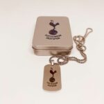 Brushed metal tin with the Tottenham Hotspur logo beside a matching silver dog tag pendant on a chain.