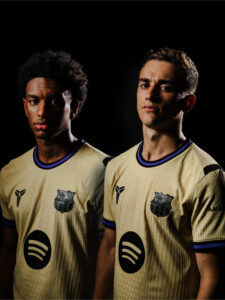 Two young male soccer players in matching beige jerseys pose side by side in a dark studio; Spotify logo visible on their shirts.