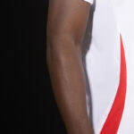 TtgLKWGTXTKTxCd | UAE SPORT STORE Close-up of a dark-skinned arm by a black background, with part of a white mesh garment and a red stripe at the edge visible to the right.