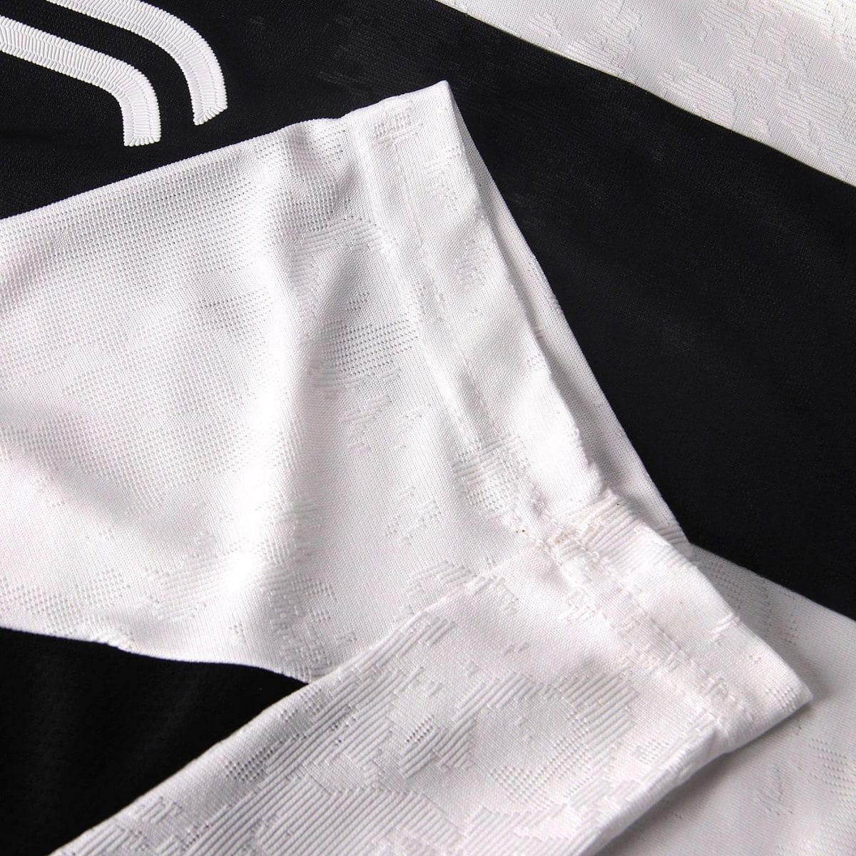 Close-up of white jacquard fabric with a subtle raised pattern laid over a black textile surface