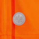 U6P4rll03A7ZDpr | UAE SPORT STORE Silver circular badge with a detailed eagle in the center pinned to bright orange fabric.