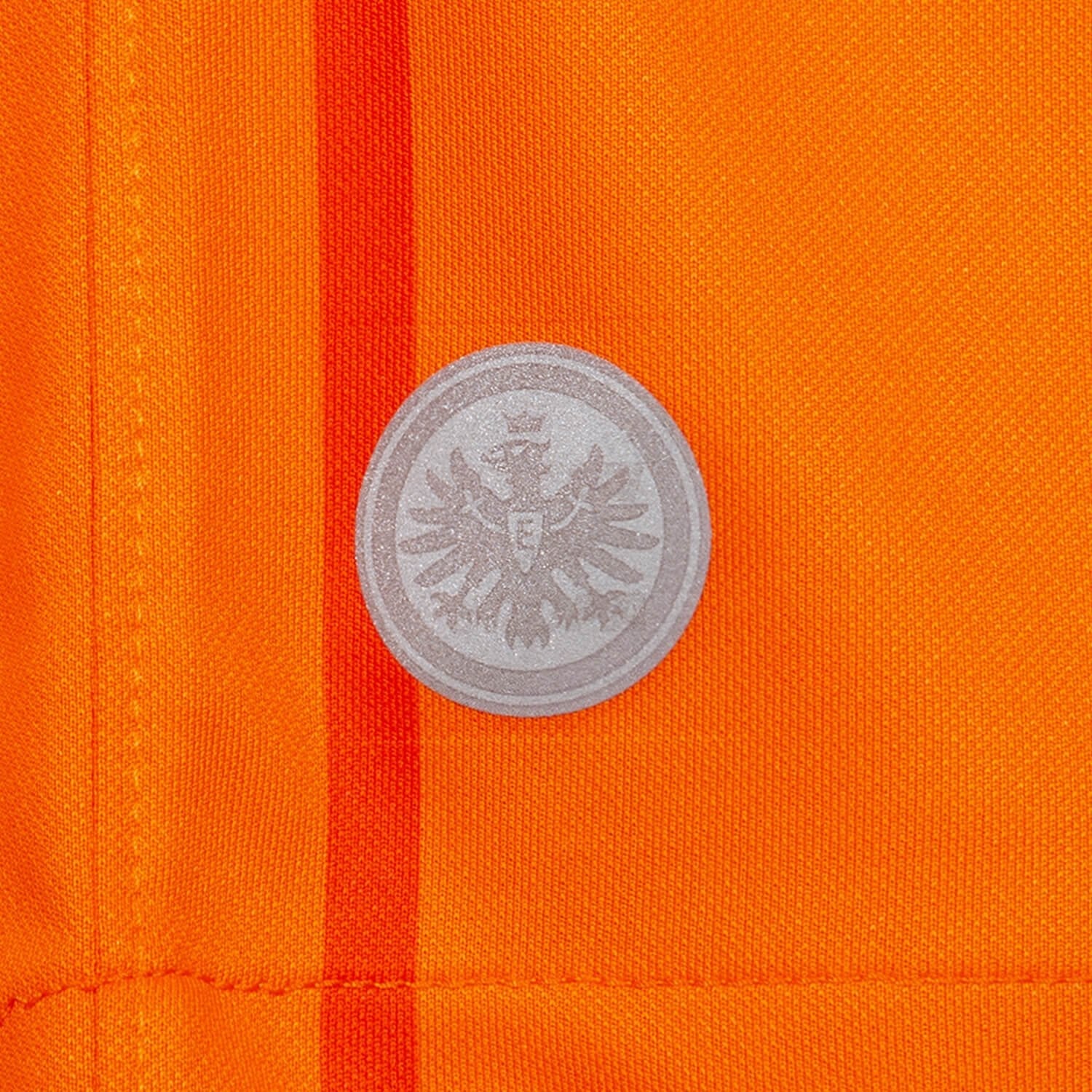 U6P4rll03A7ZDpr | UAE SPORT STORE Silver circular badge with a detailed eagle in the center pinned to bright orange fabric.