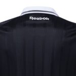 UK | UAE SPORT STORE Back view of a dark, vertically striped jacket or shirt with a white collar featuring the white 'Reebok' logo.