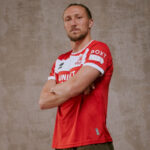 Athlete in a red jersey posing with arms crossed, looking at the camera against a neutral backdrop.