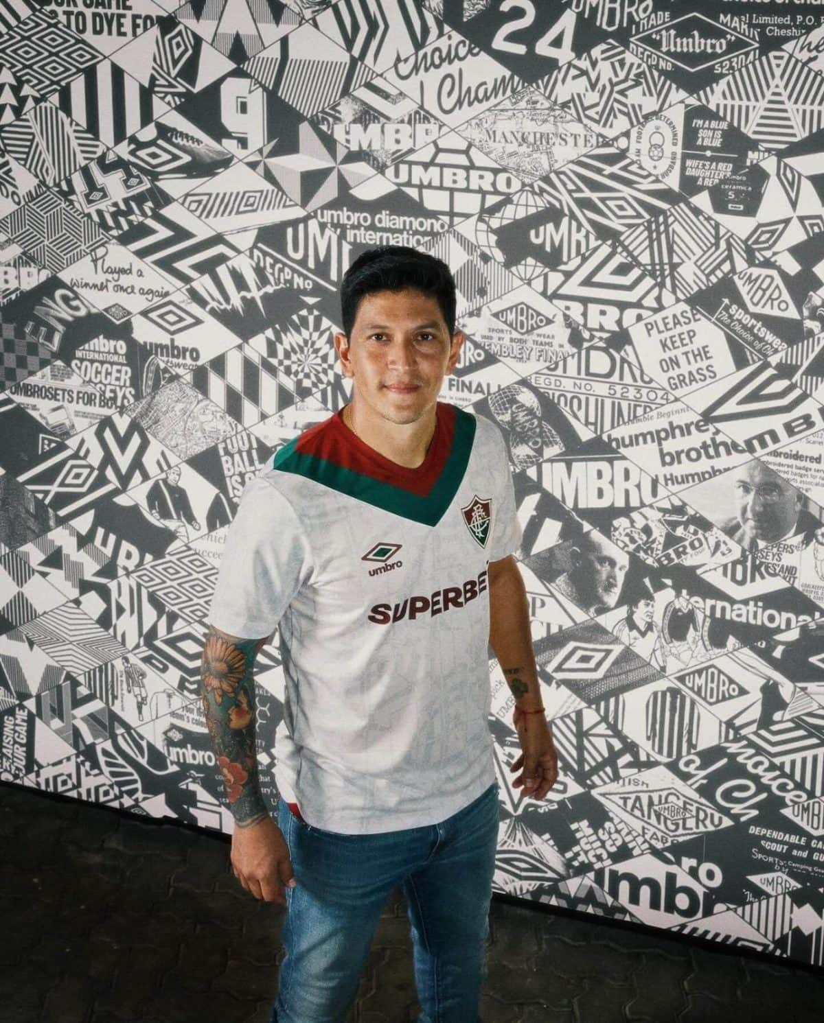 Man wearing a white Flamengo football jersey stands against a black-and-white collage wall featuring logos and patterns.