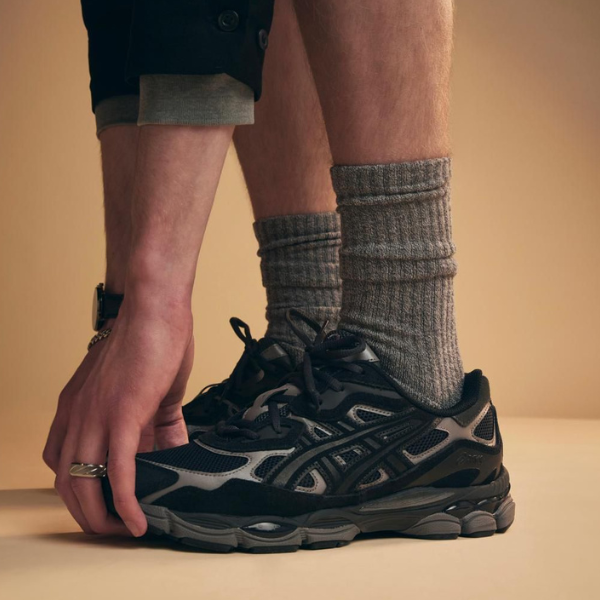 Person tying the laces of a dark athletic sneaker while wearing thick gray socks.