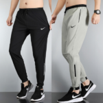 Side-by-side view of two men's Nike jogger pants: black pair on the left and light gray pair on the right, with logo and zip pockets visible.