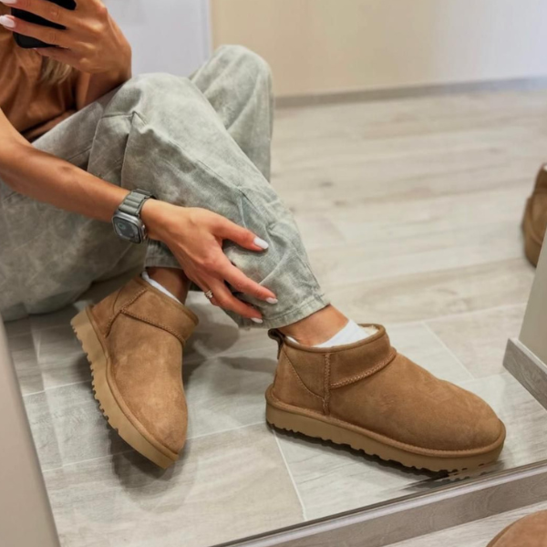 Person sitting on a tiled floor wearing tan suede ankle boots with white socks, taking a mirror selfie.