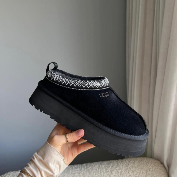 Black UGG slip-on platform boot with a white knit collar, held in a hand indoors.