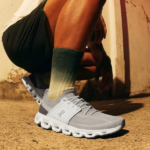 Untitled_design_-_2025-01-14T221547.126 | UAE SPORT STORE Person crouching on a sunlit concrete surface, wearing gray running shoes and olive-green socks.