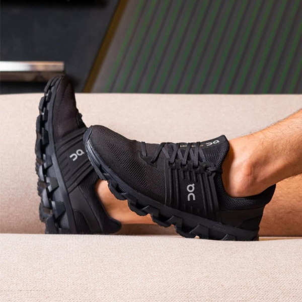 Black athletic running shoes with chunky soles resting on a beige sofa surface, laces tied.
