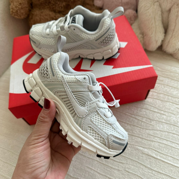 Pair of white sporty sneakers with chunky soles next to a red Nike shoebox, shown from a close-up angle for scale and detail.