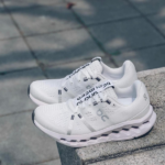 Pair of white athletic running shoes with chunky soles resting on a concrete step.