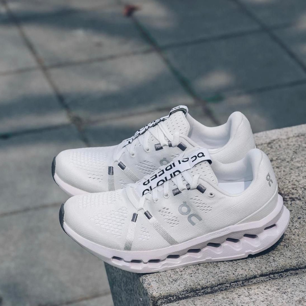 Pair of white athletic running shoes with chunky soles resting on a concrete step.