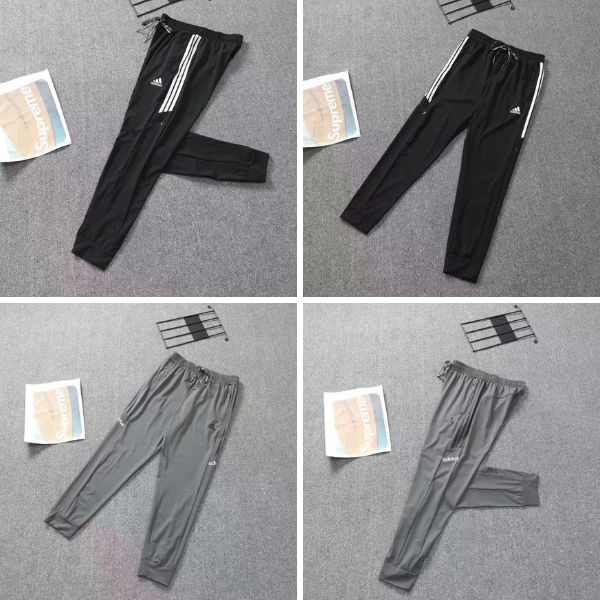 Black Adidas track pants with white stripes along the side, laid flat on a gray carpet with a magazine nearby.