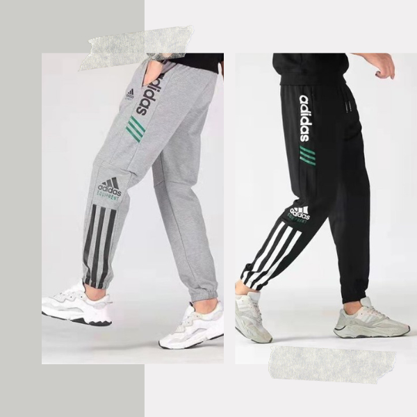 Two people modeling Adidas track pants: gray pair with black stripes and logo, and black pair with white stripes and logo.