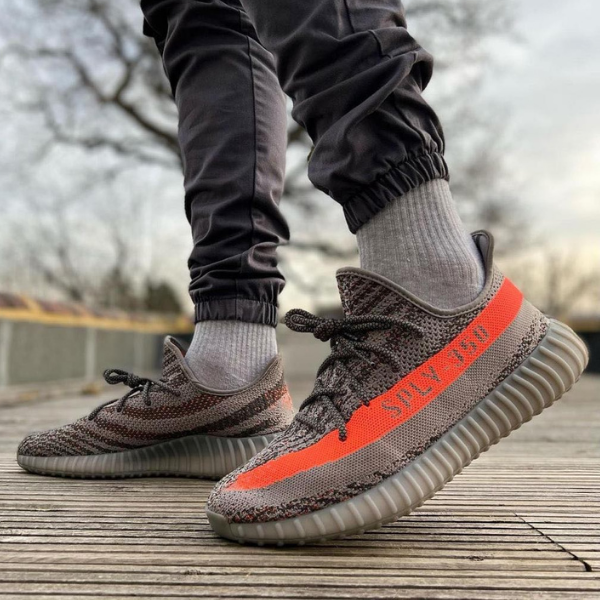Person wearing gray knit sneakers with an orange SPLY-350 stripe, standing on a wooden deck.