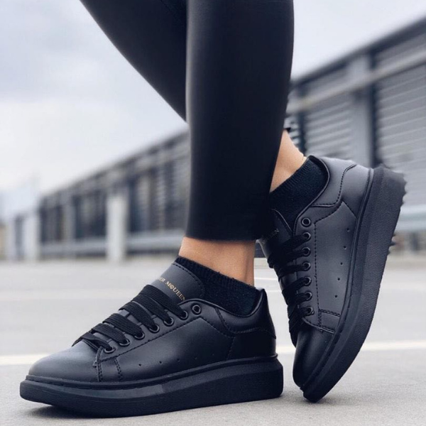Black sneakers with matching black leggings worn on a paved outdoor surface, urban backdrop in the distance.