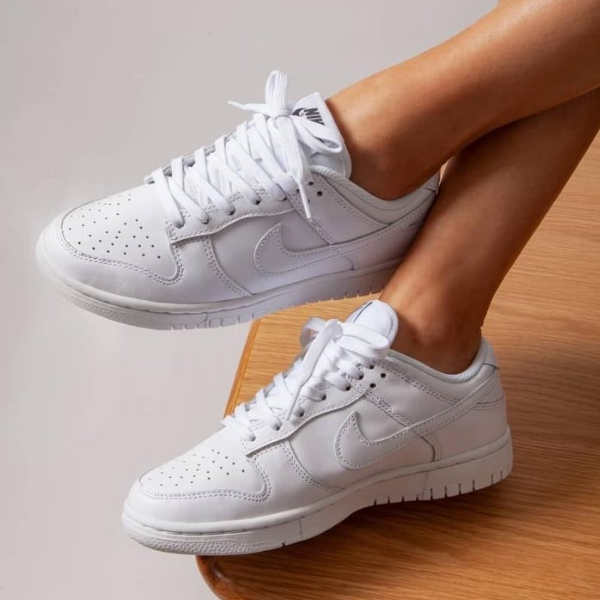 Pair of white sneakers on a person’s feet, resting on a wooden step, showing the Nike swoosh and laces.