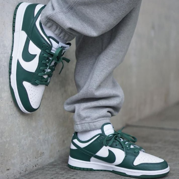 Close-up of green and white Nike sneakers worn with gray sweatpants, against a concrete wall.
